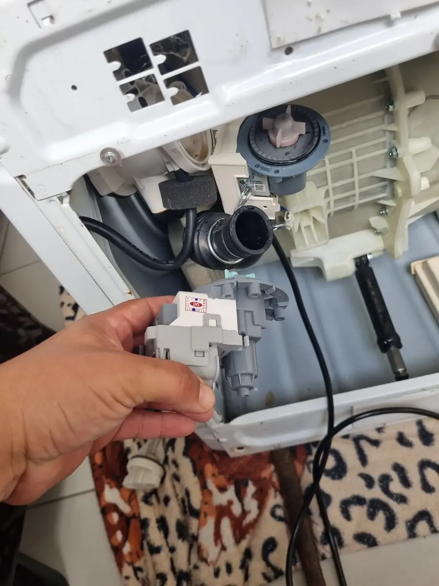 Técnico segurando a eletrobomba de drenagem retirada de uma lavadora Samsung
